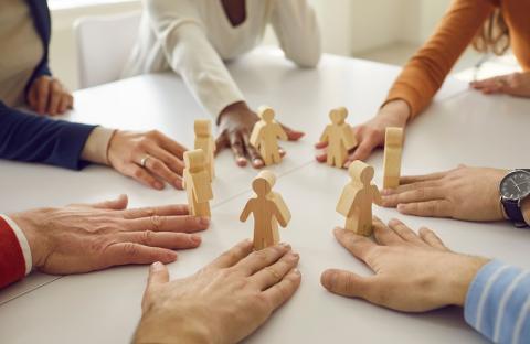 hands, each bringing a wooden person to the table