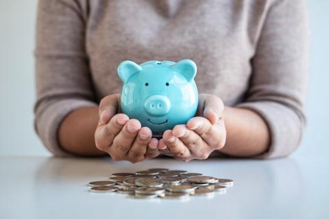 person holding piggy bank with coins on table
